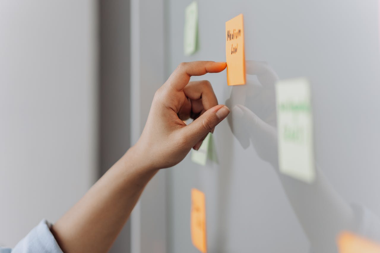About A hand placing a sticky note on a reflective surface in an office setting.