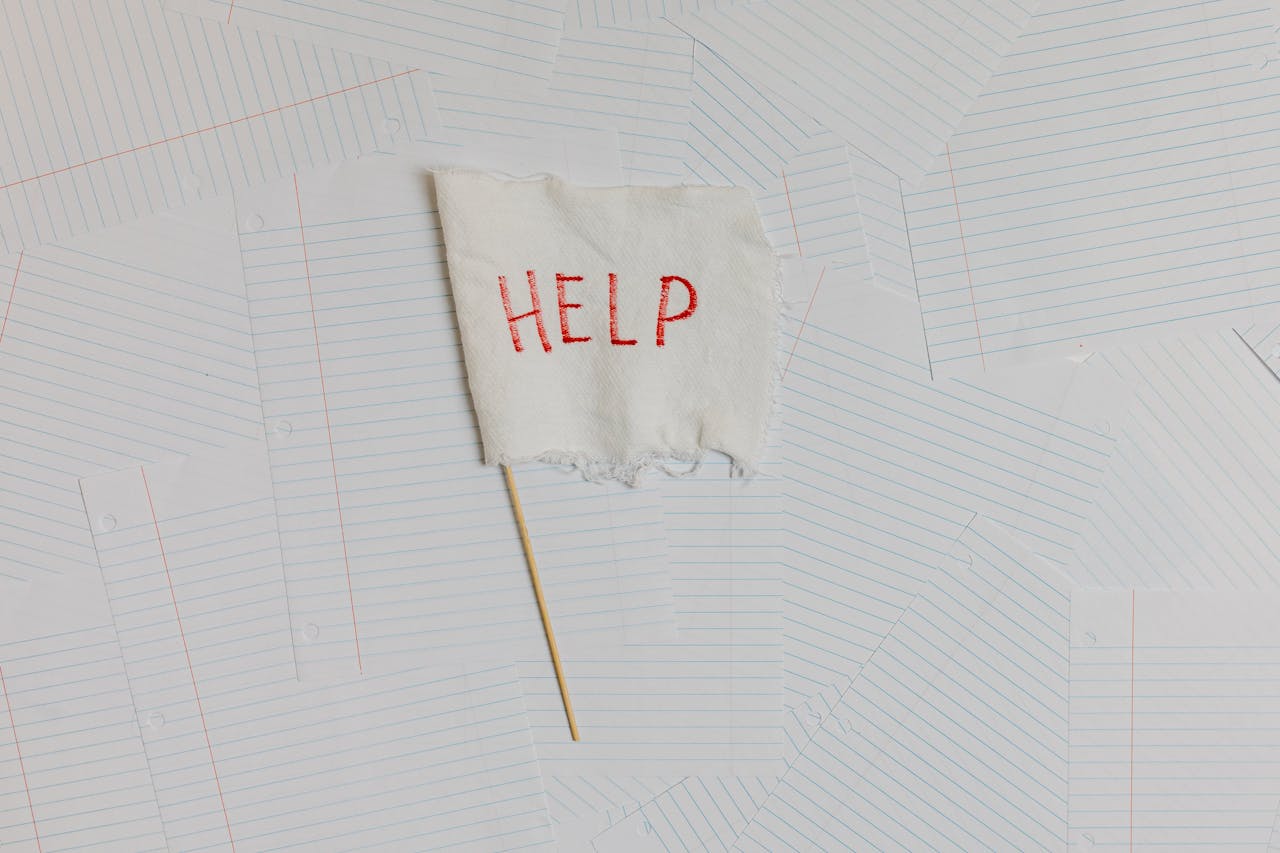 A fabric flag with 'HELP' on a scattered notepaper background, symbolizing distress or overwhelm.